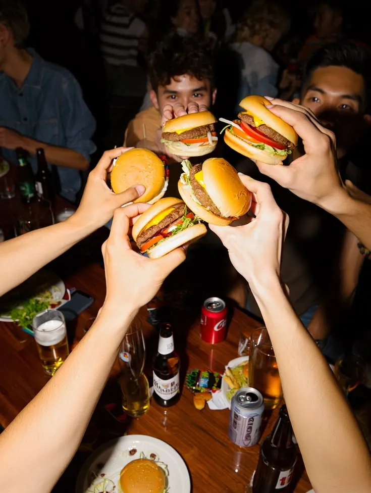 Four people holding cheeseburgers up over a table